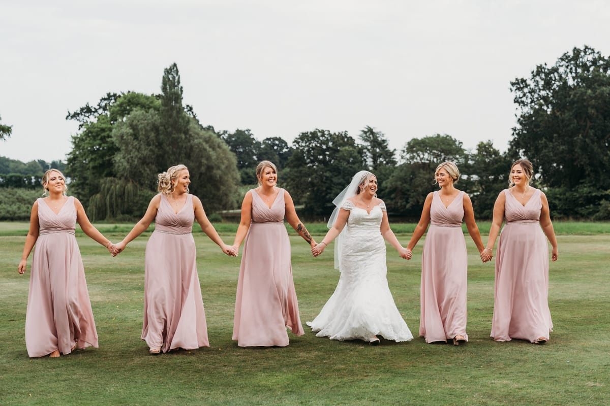 bride walks across the garden to the rear of Norwood park holding hands with her 5 bridesmaids dressed in dusky pink dresses