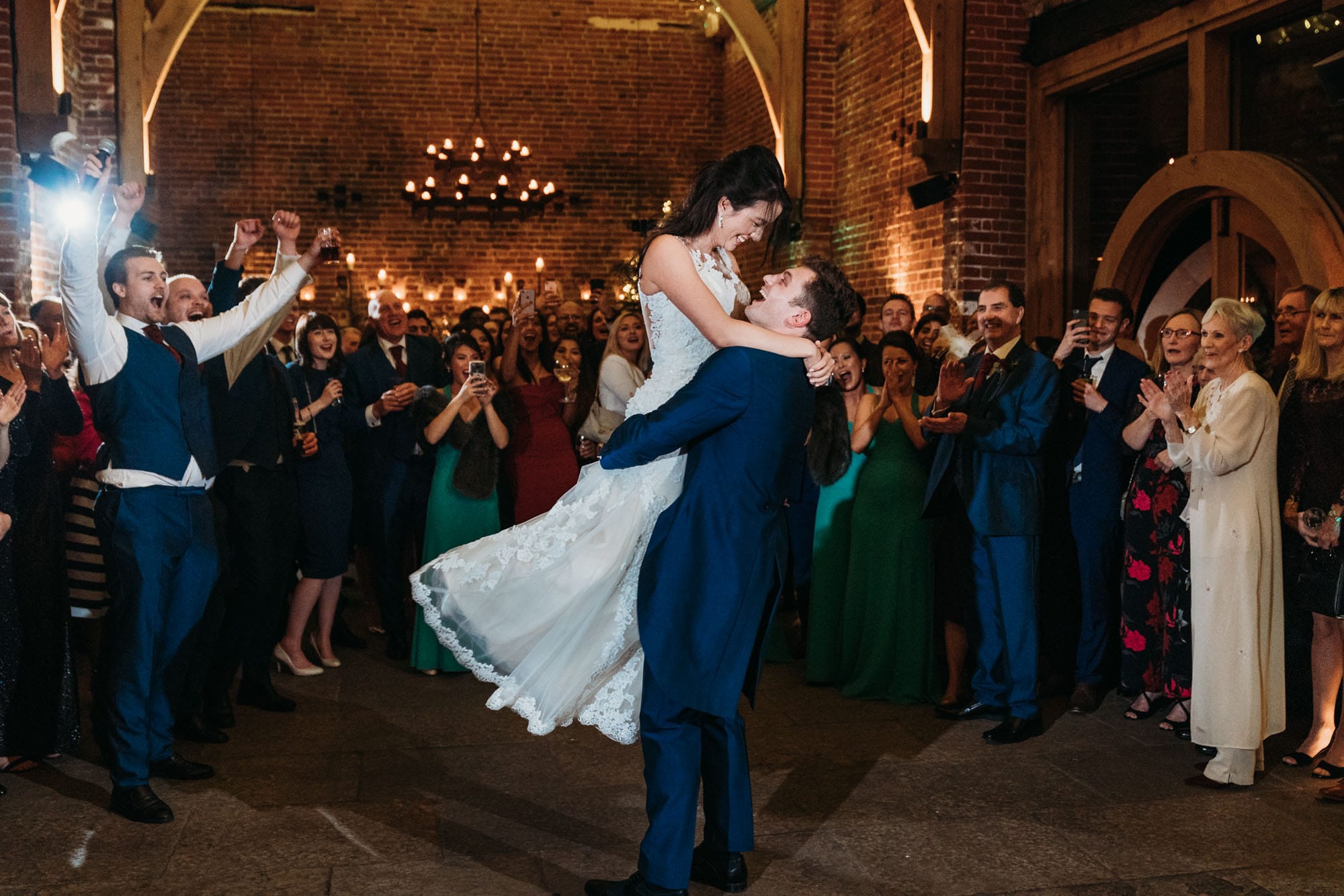 groom picks bride up during first dance for a spin. Guests look on clapping and cheering