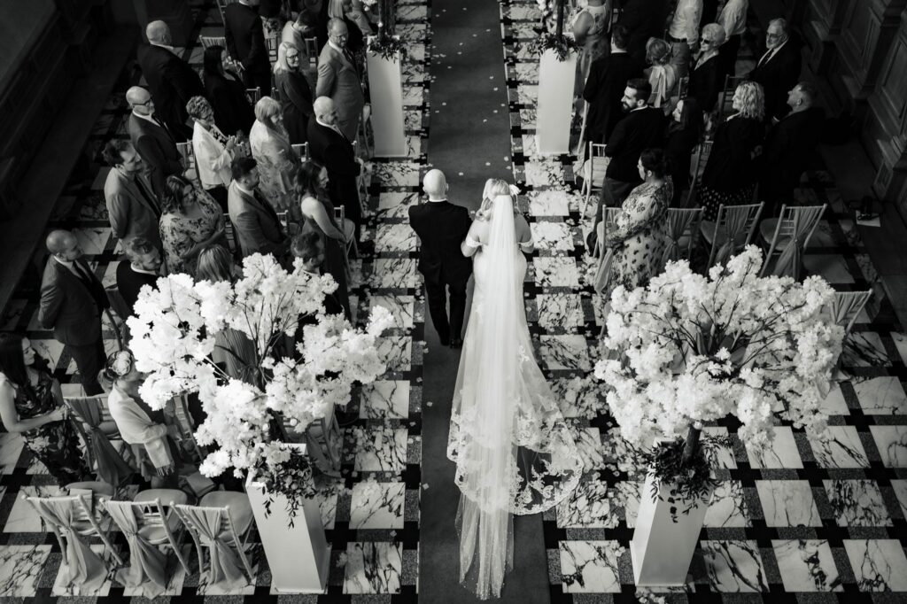 black and white photo of bride as she walks down the aisle at Harlaxton Manor from the gallery upstairs