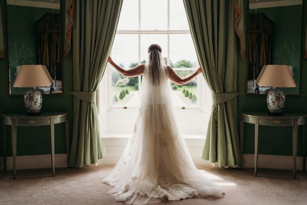 bride standing in the window of bridal suite at Stubton Hall with rear of dress showing