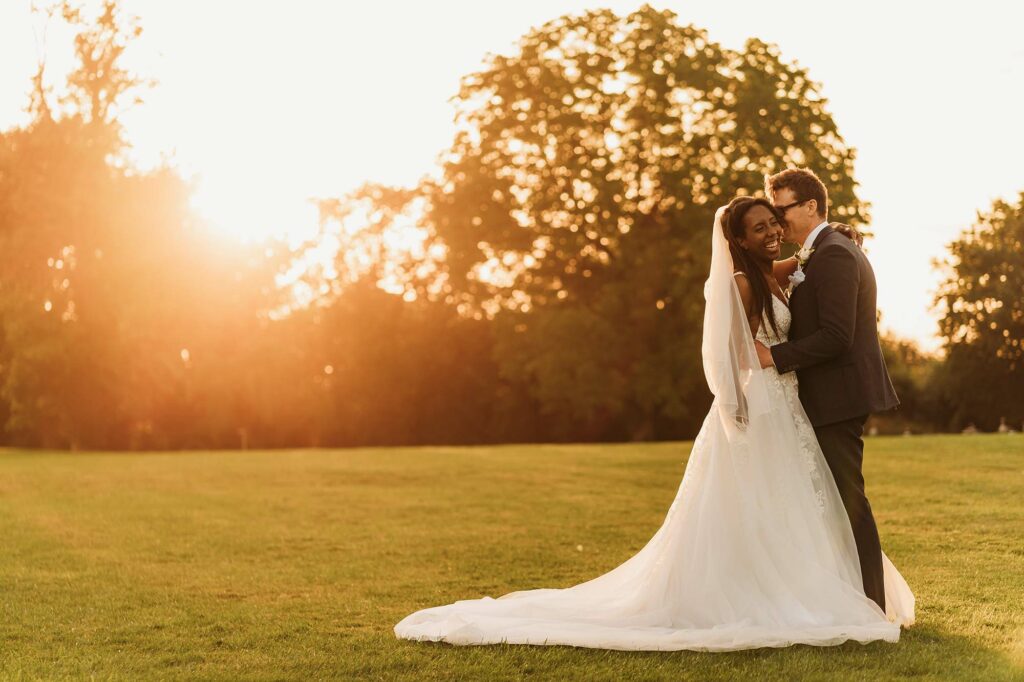 bride laughing with groom during golden hour wedding session with sun flare behind them