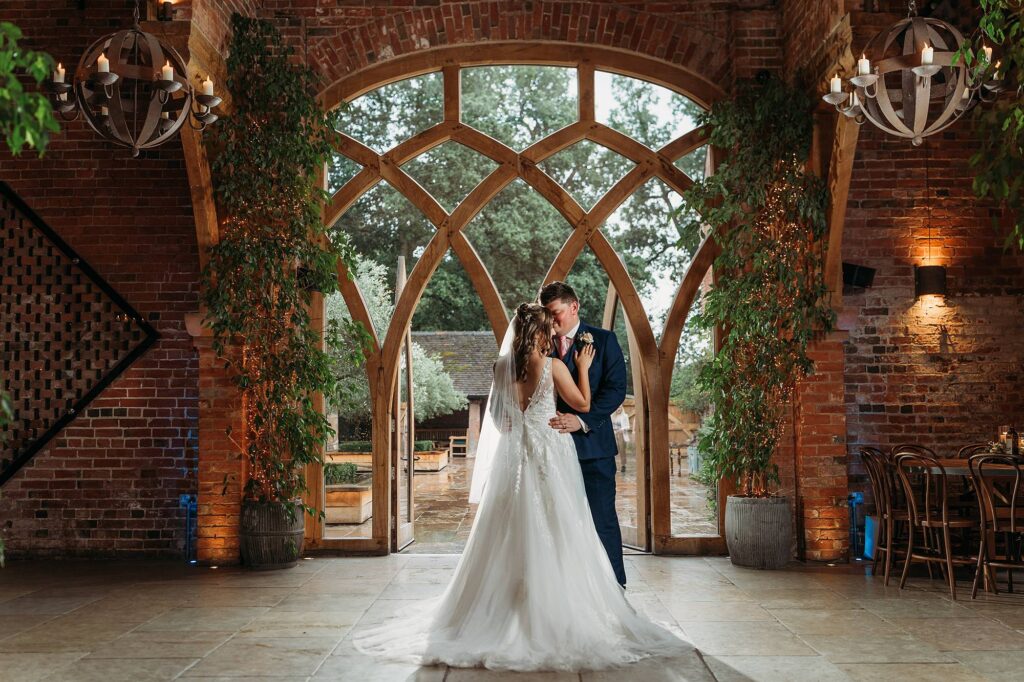 Indoor flash wedding photograph of bride and groom inside the barn next to the large barn doors at Shustoke Barn