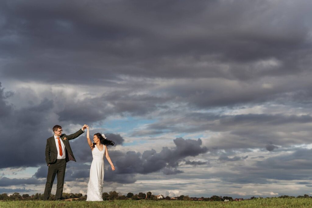 Chloe & Ben twirling with a beautiful sky behind them at their wedding in Grangefields