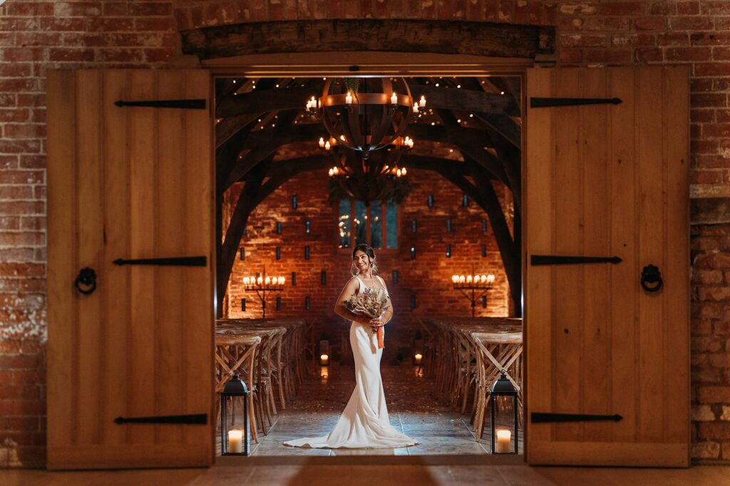 Beautiful bride in the ceremony room at Grangefields in the evening with the candles lit, holding her bouquet, looking to the right