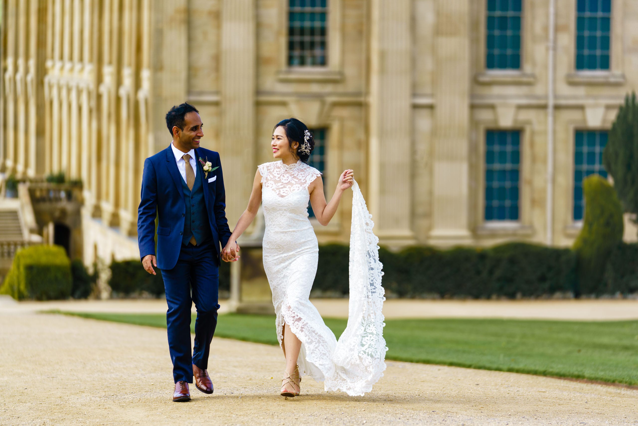 Newlywed Bride & Groom walking hand in hand with Chatsworth House behind them