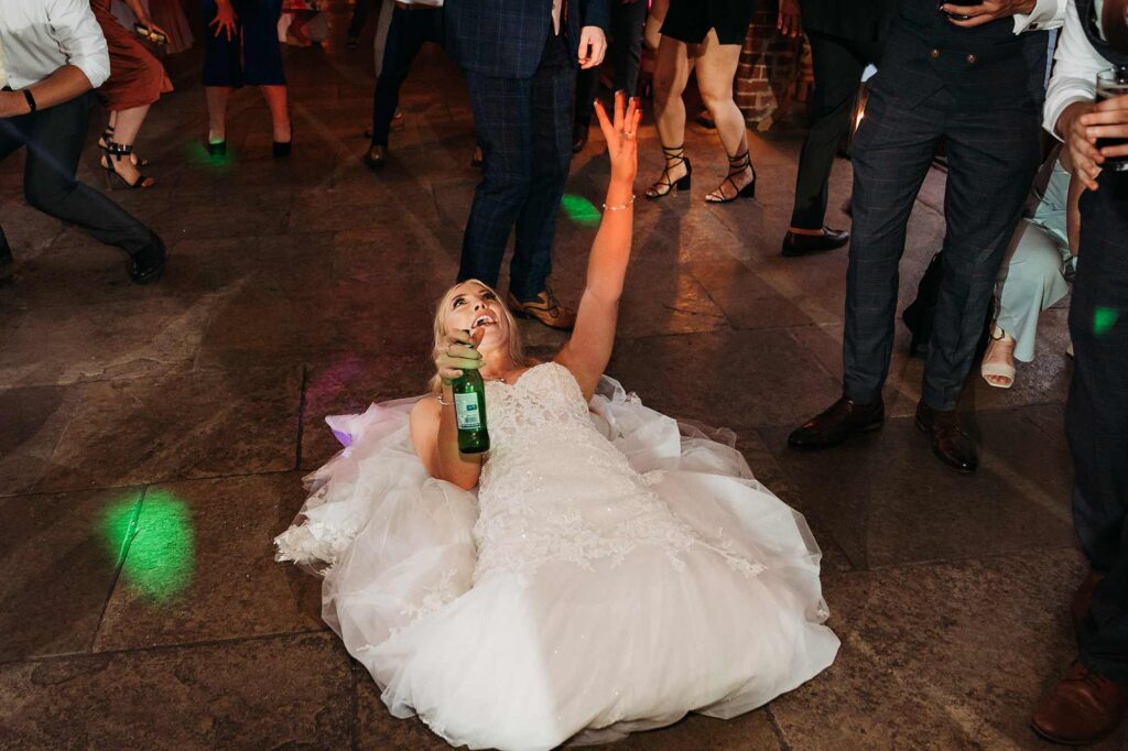 Bride lying on her back on the dancefloor with a bottle of beer in hand