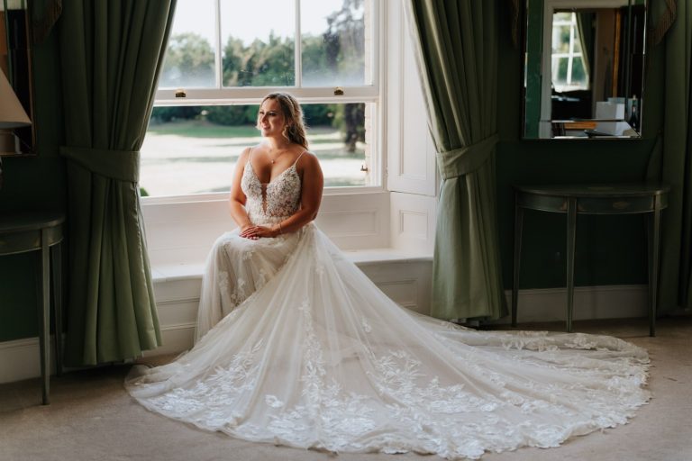 Bride sitting at window in the bridal suite at Stubton Hall with beautiful train flowing